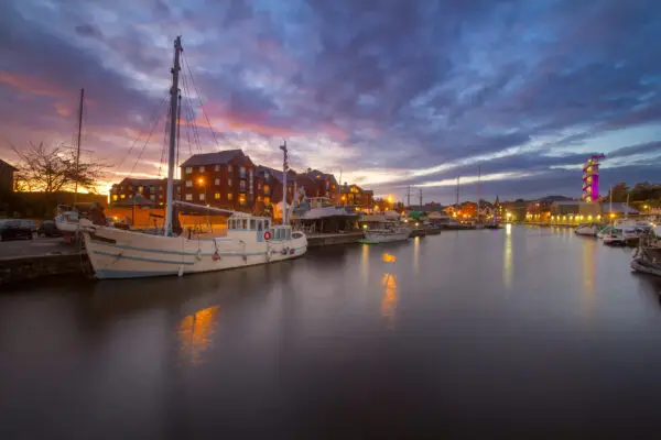 A white masted vessel is moored in a harbor in the city of Exeter. Other vessels are also visible. Colorful sunset. Exeter. Devon. England